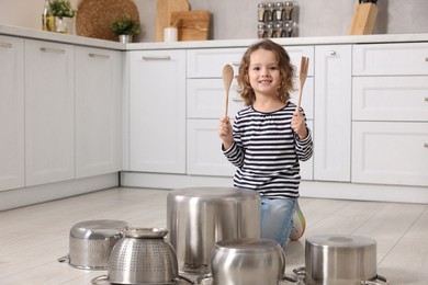 Little girl pretending to play drums on pots in kitchen