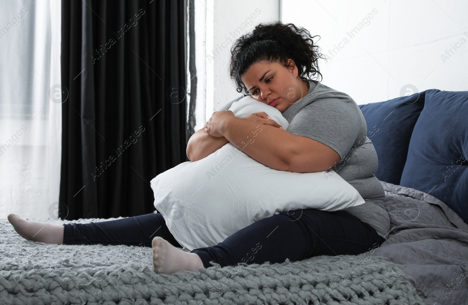 Photo of Depressed overweight woman hugging pillow on bed