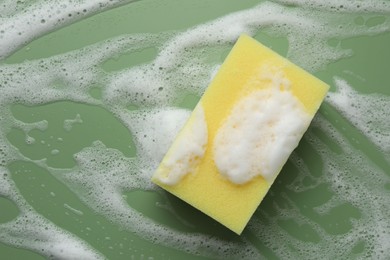 Yellow sponge with foam on green background, top view