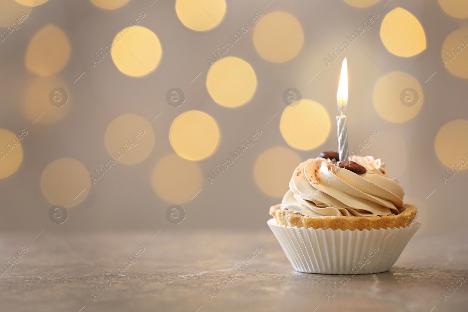 Photo of Tasty birthday cupcake with candle on table against blurred lights, space for text