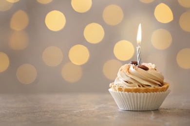 Tasty birthday cupcake with candle on table against blurred lights, space for text