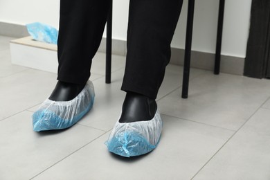 Photo of Woman wearing blue shoe covers onto her boots indoors, closeup