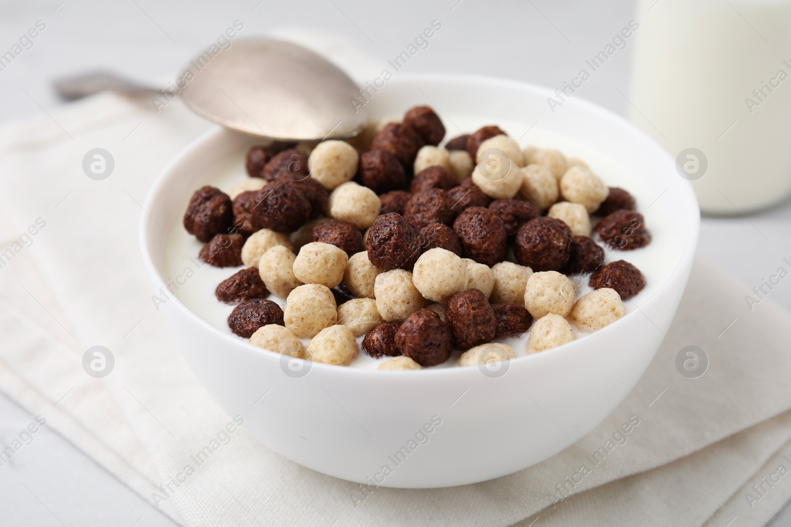 Photo of Breakfast cereal. Tasty corn balls with milk in bowl and spoon on table, closeup