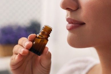Photo of Woman with bottle of essential oil indoors, closeup