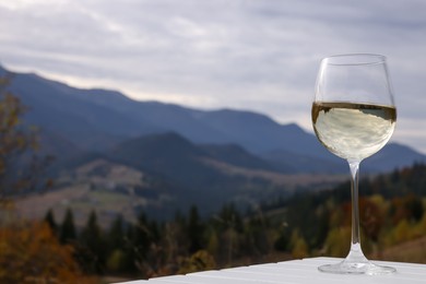 Glass of tasty wine on white wooden table against mountain landscape. Space for text