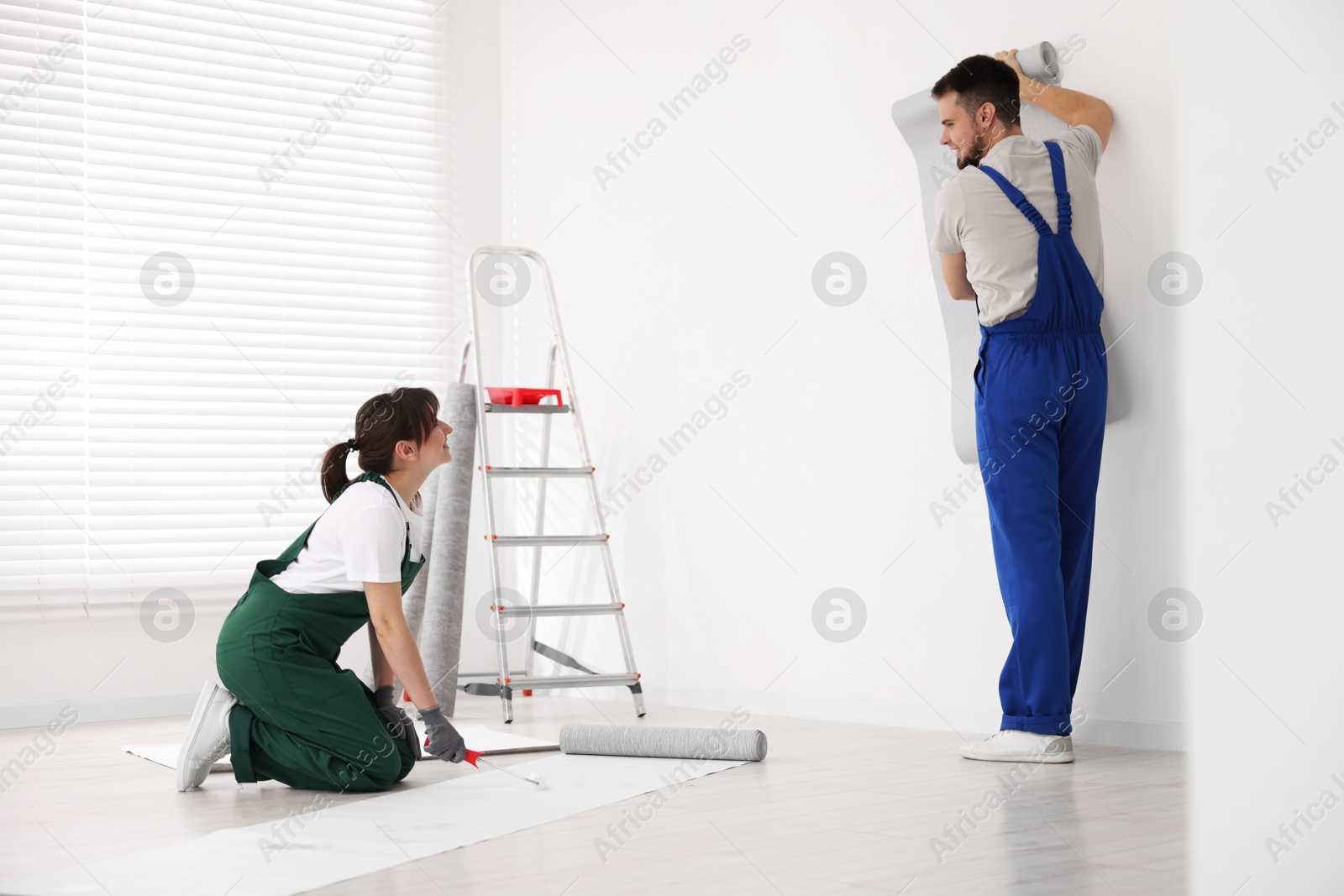 Photo of Woman applying glue onto wallpaper while man hanging sheet indoors