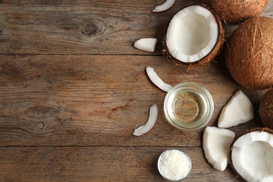 Bowl of natural organic oil and coconuts on brown wooden background, flat lay. Space for text