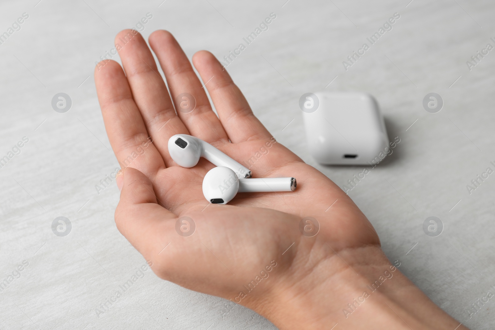 Photo of Woman with wireless earphones and charging case at light table, closeup