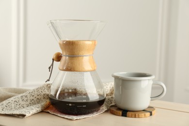 Glass chemex coffeemaker with coffee and cup on table