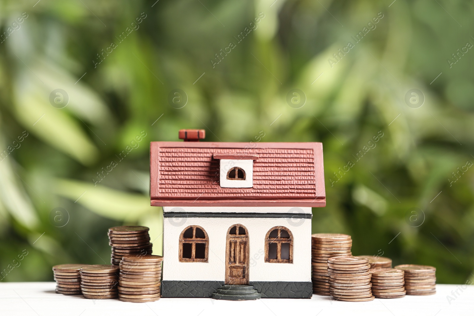 Photo of House model and coins on white table against blurred green background