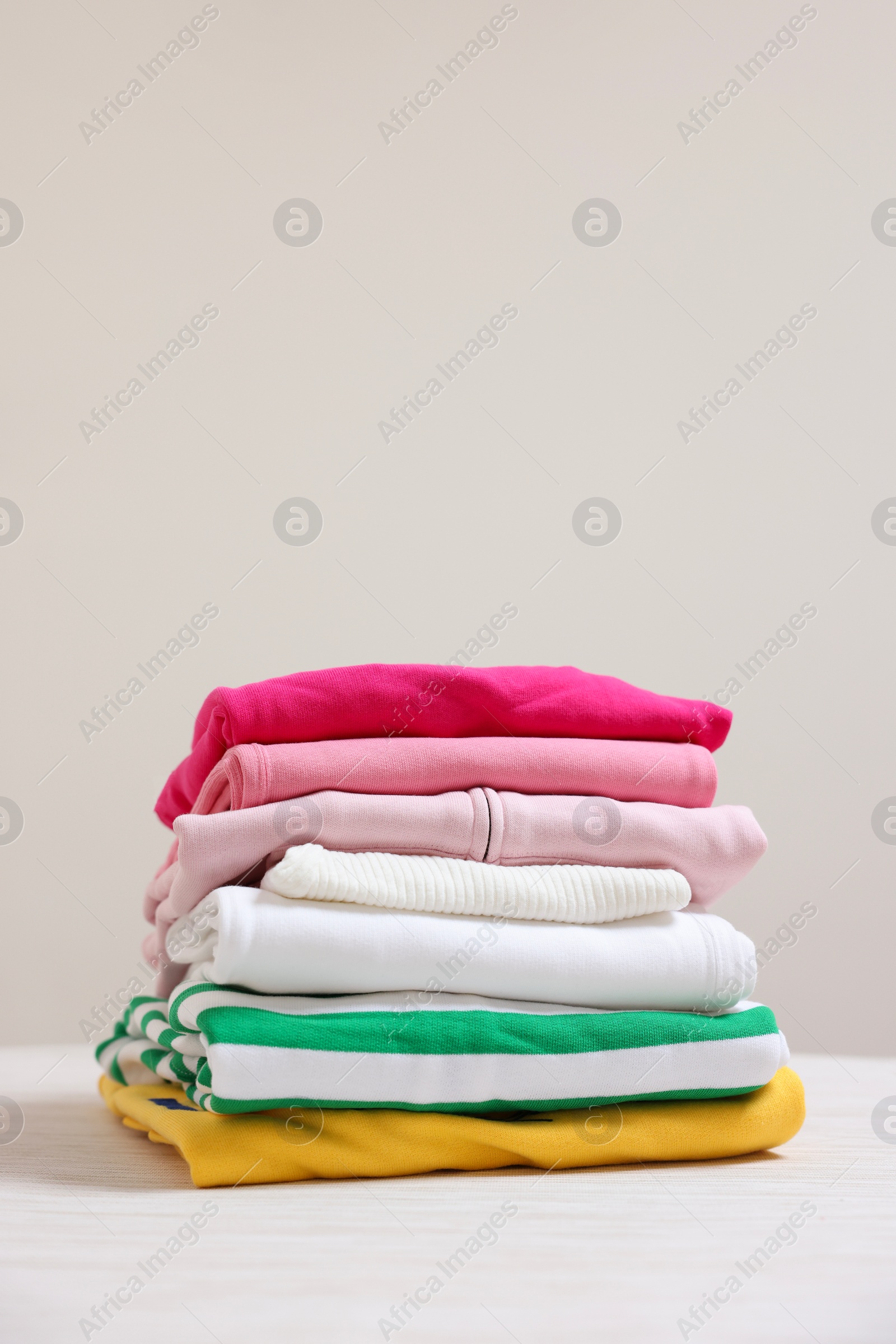 Stack of folded clothes on table against beige background Photo of Stack of folded clothes on table against beige background