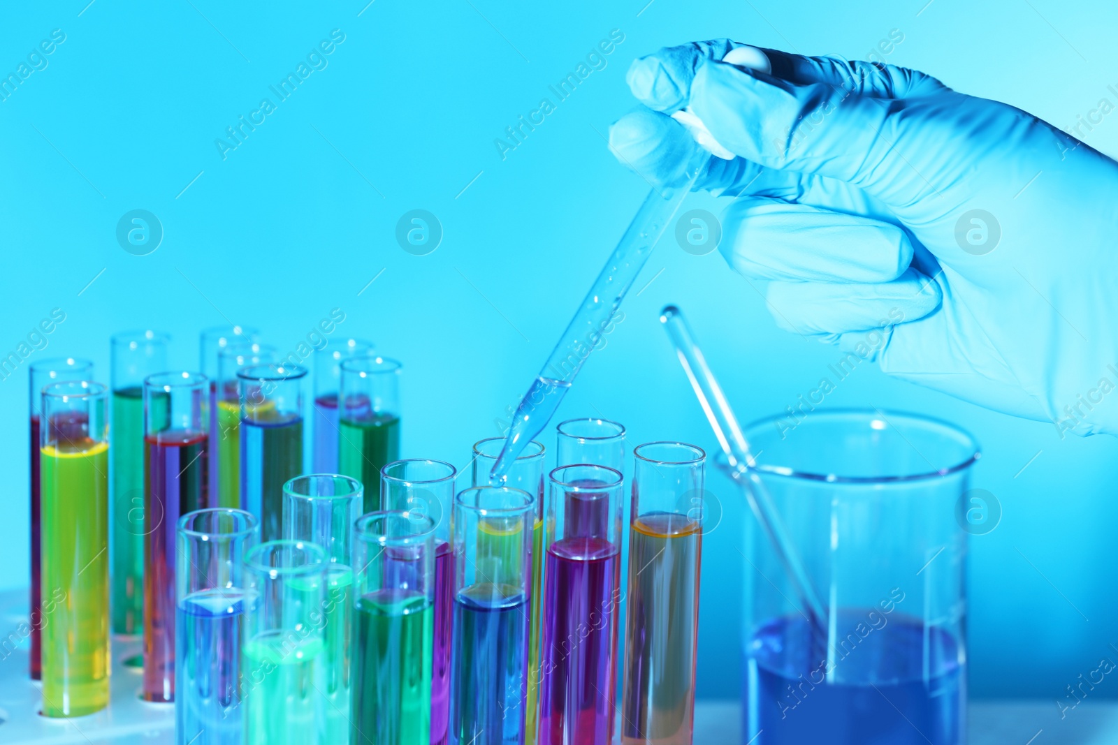 Photo of Scientist dripping liquid from pipette into test tube on light blue background, closeup