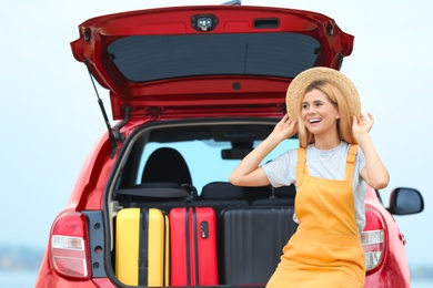 Happy woman near car trunk with suitcases outdoors