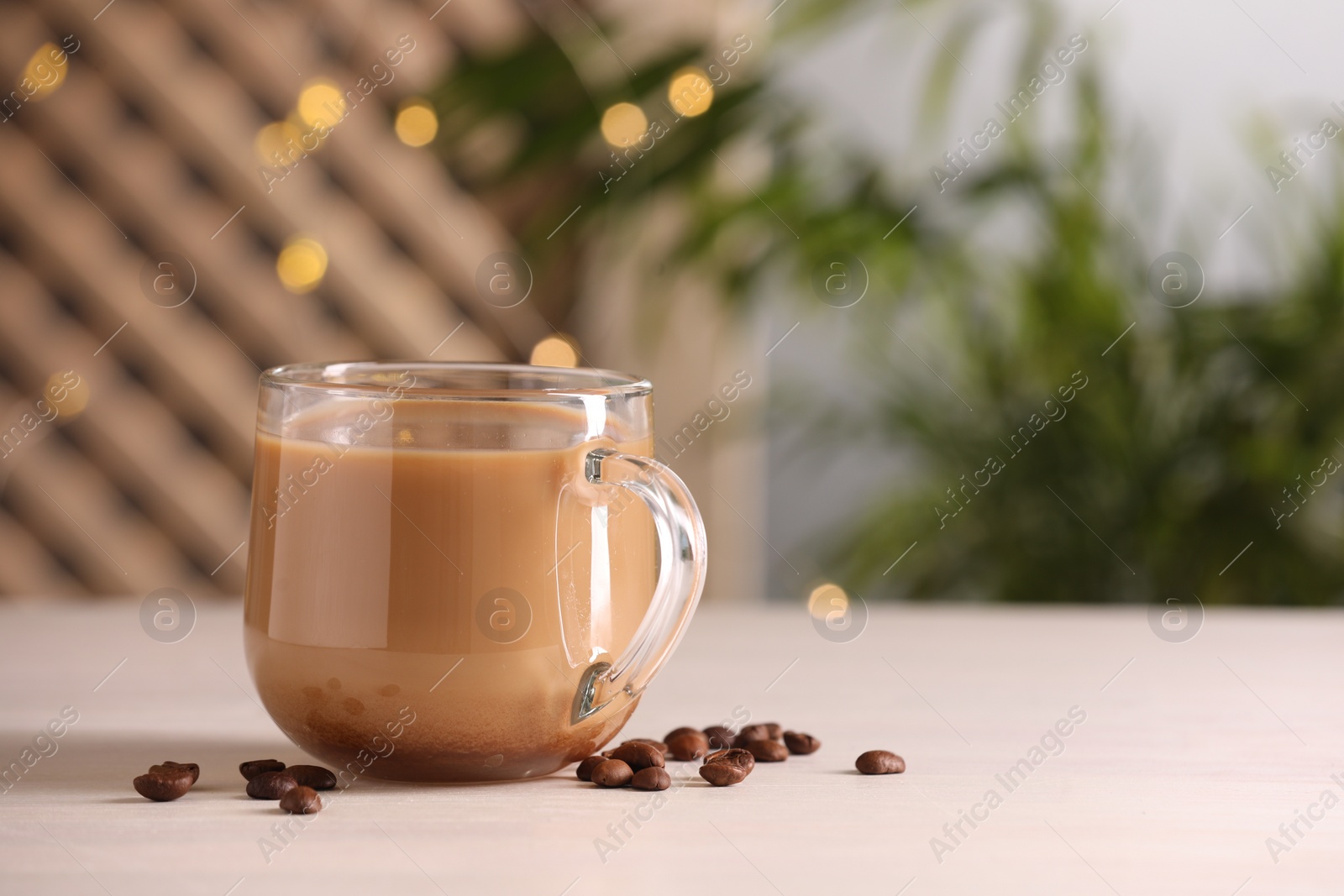 Photo of Delicious coffee with milk in cup and beans on white wooden table, closeup. Space for text