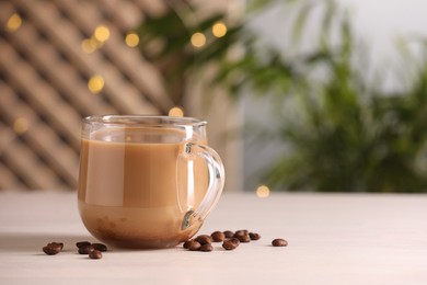 Delicious coffee with milk in cup and beans on white wooden table, closeup. Space for text