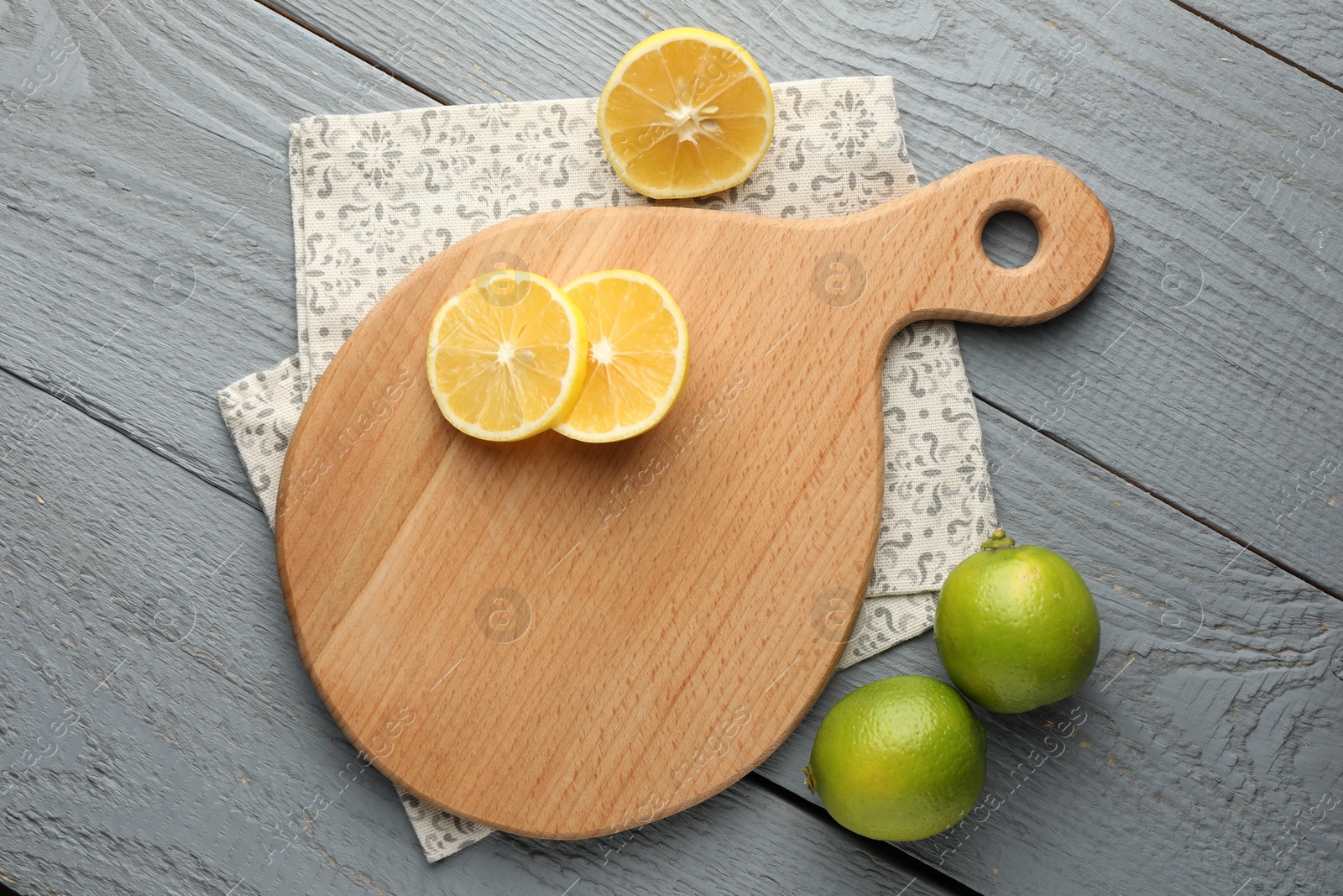 Photo of Cutting board, lemon and limes on grey wooden table, flat lay