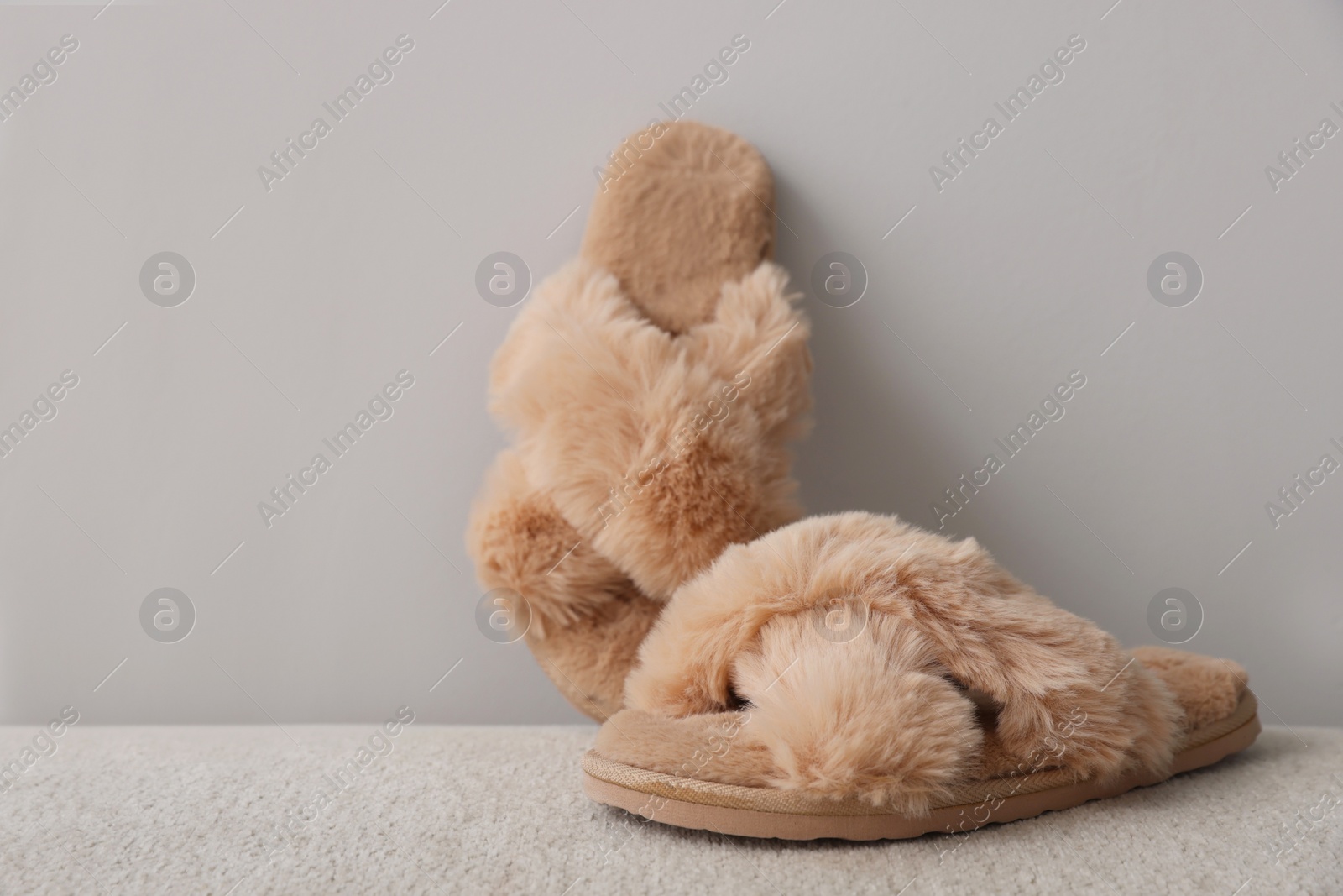 Photo of Soft beige slippers near grey wall, space for text