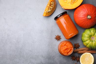 Jars of pumpkin jam and ingredients on grey table, flat lay. Space for text