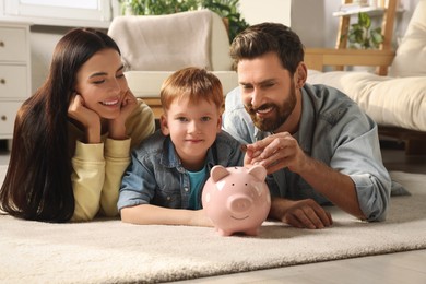 Photo of Happy family with ceramic piggy bank on floor at home