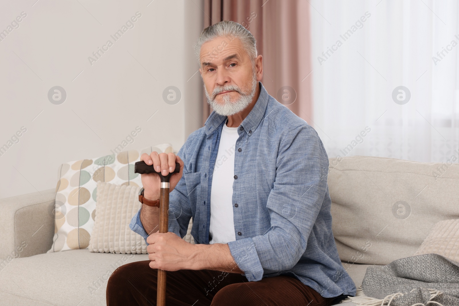 Photo of Senior man with walking cane sitting on sofa at home