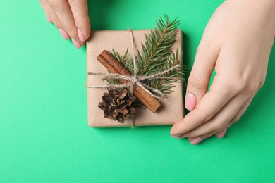 Woman with beautifully wrapped Christmas gift box on green background, top view