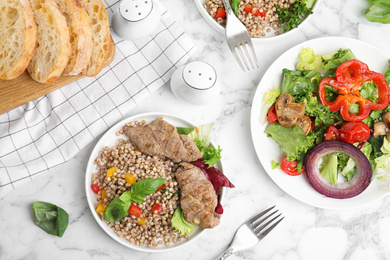 Tasty buckwheat porridge with meat on white marble table, flat lay