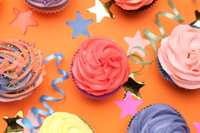 Photo of Delicious cupcakes with bright cream and party decor on orange background, flat lay