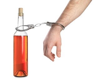 Photo of Addicted man in handcuffs with bottle of alcoholic drink on white background, closeup