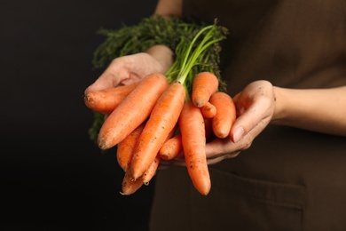 Young woman holding ripe carrots on black background, closeup