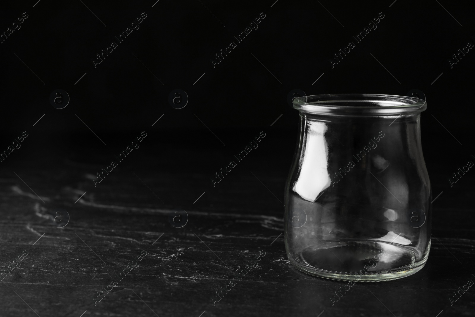 Photo of Empty glass jar on black stone table, space for text