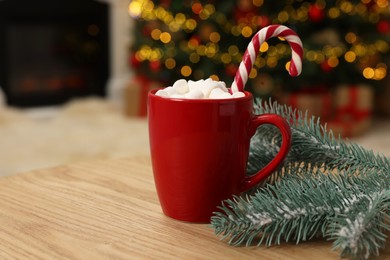 Christmas cocoa with marshmallows and candy cane in red cup on wooden table indoors, closeup