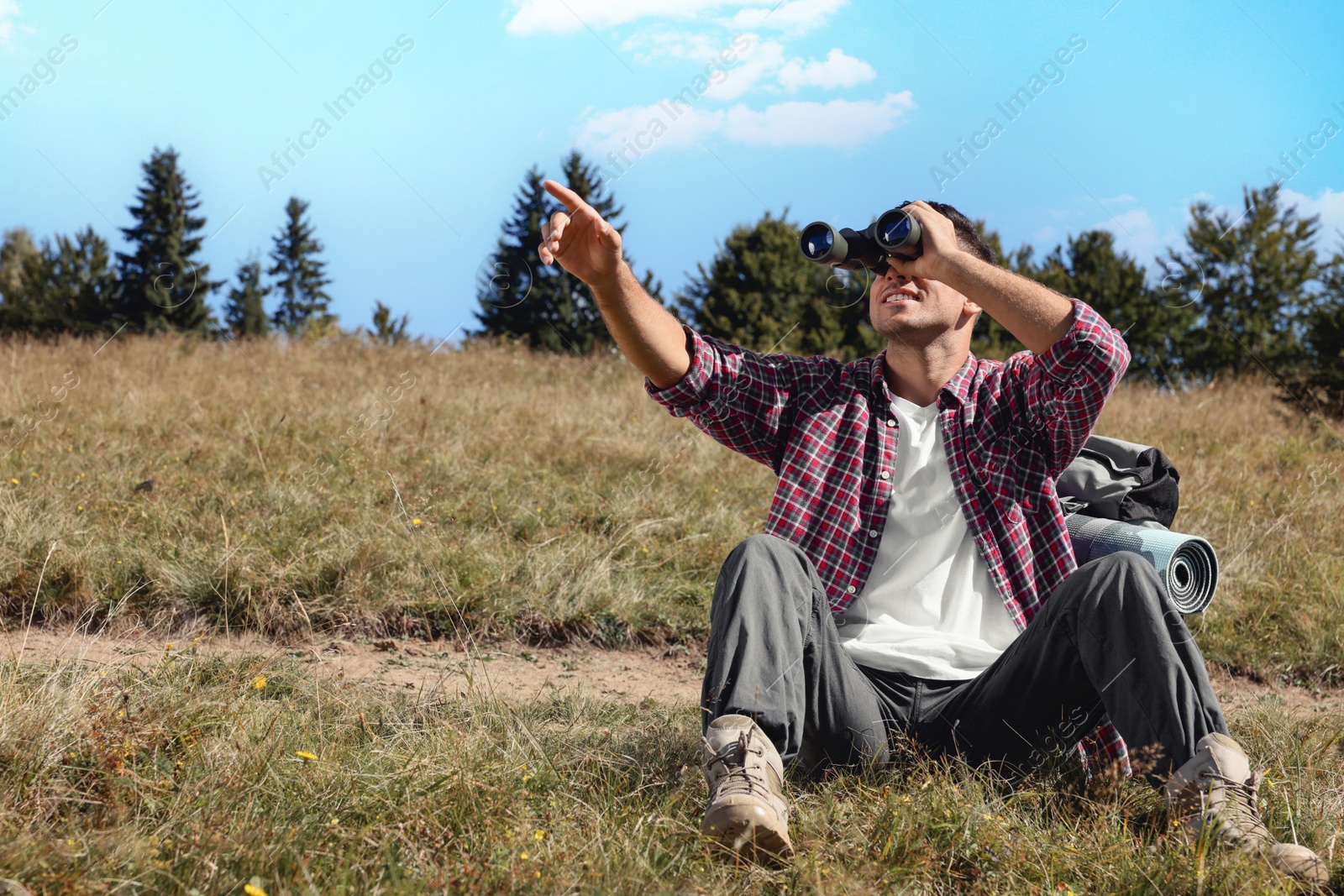 Photo of Tourist with hiking equipment looking through binoculars outdoors