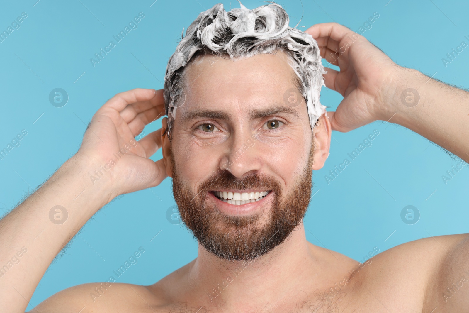 Photo of Happy man washing his hair with shampoo on light blue background, closeup