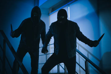 Men in masks with knives on stairs indoors. Dangerous criminals