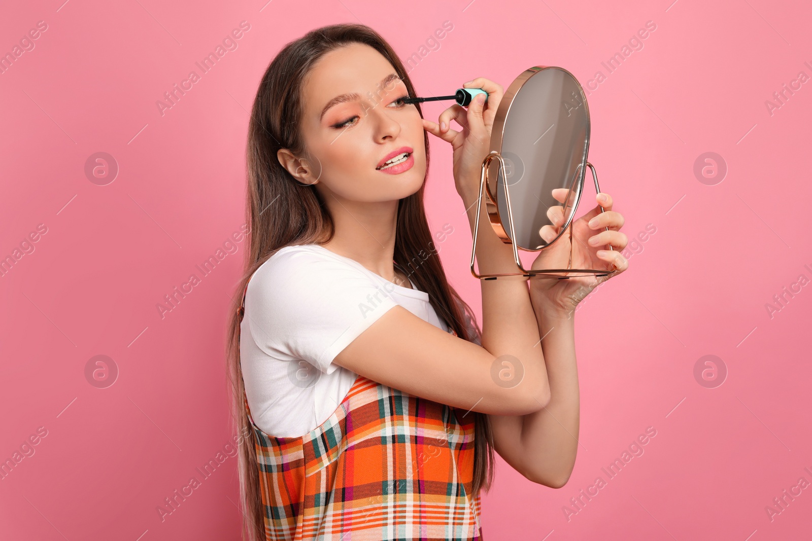 Photo of Beauty blogger applying mascara on pink background