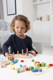 Photo of Motor skills development. Little girl playing with stacking and counting game at table indoors