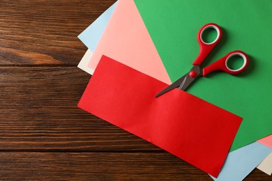 Red scissors and color paper on wooden table, flat lay. Space for text