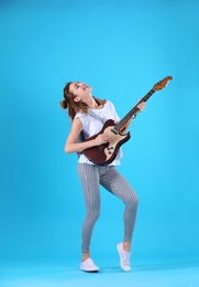 Young woman playing electric guitar on color background