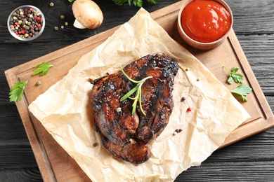 Board with barbecued steak and sauce on wooden background, top view