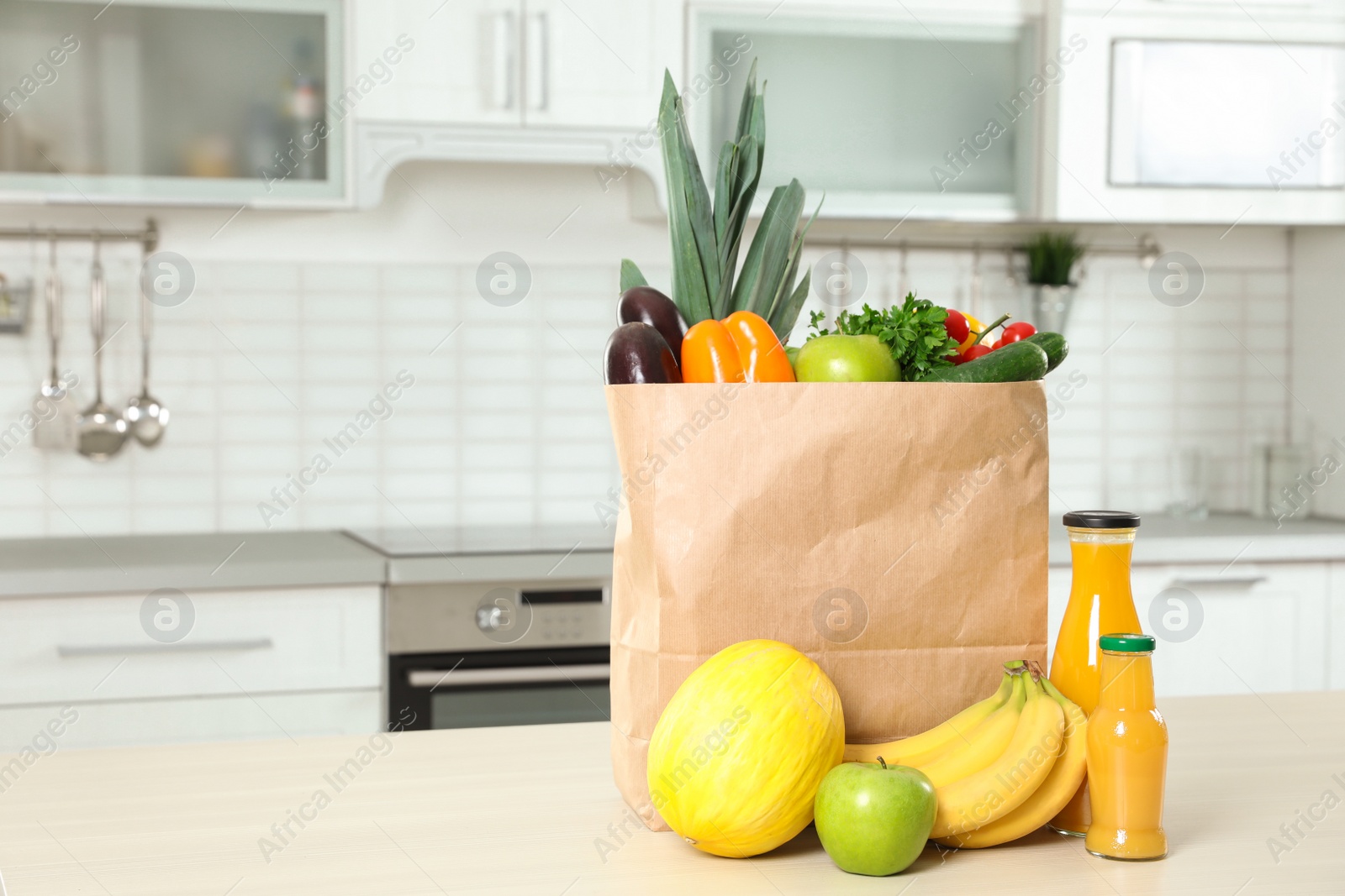 Photo of Paper shopping bag full of vegetables with fruits and juice on table in kitchen. Space for text