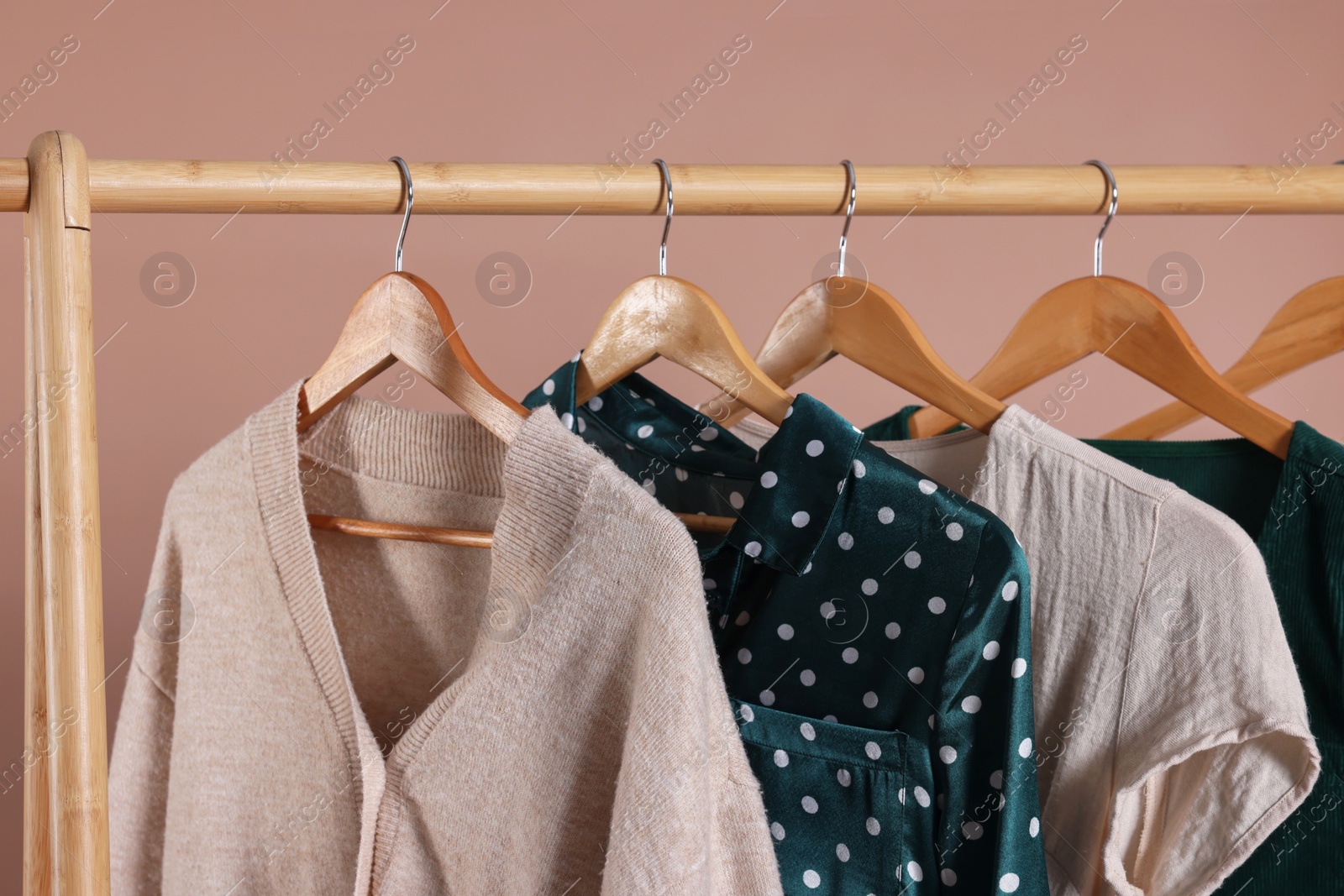 Photo of Rack with stylish women`s clothes on wooden hangers against beige background