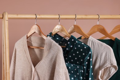 Photo of Rack with stylish women`s clothes on wooden hangers against beige background