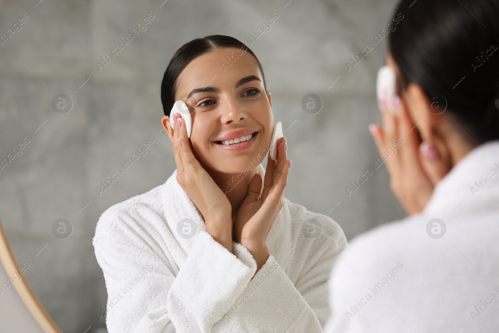 Photo of Beautiful woman removing makeup with cotton pads near mirror indoors