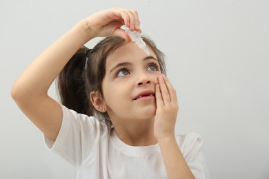 Photo of Adorable little girl using eye drops on white background