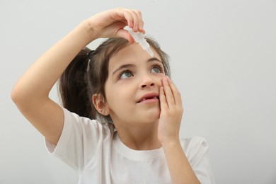 Adorable little girl using eye drops on white background