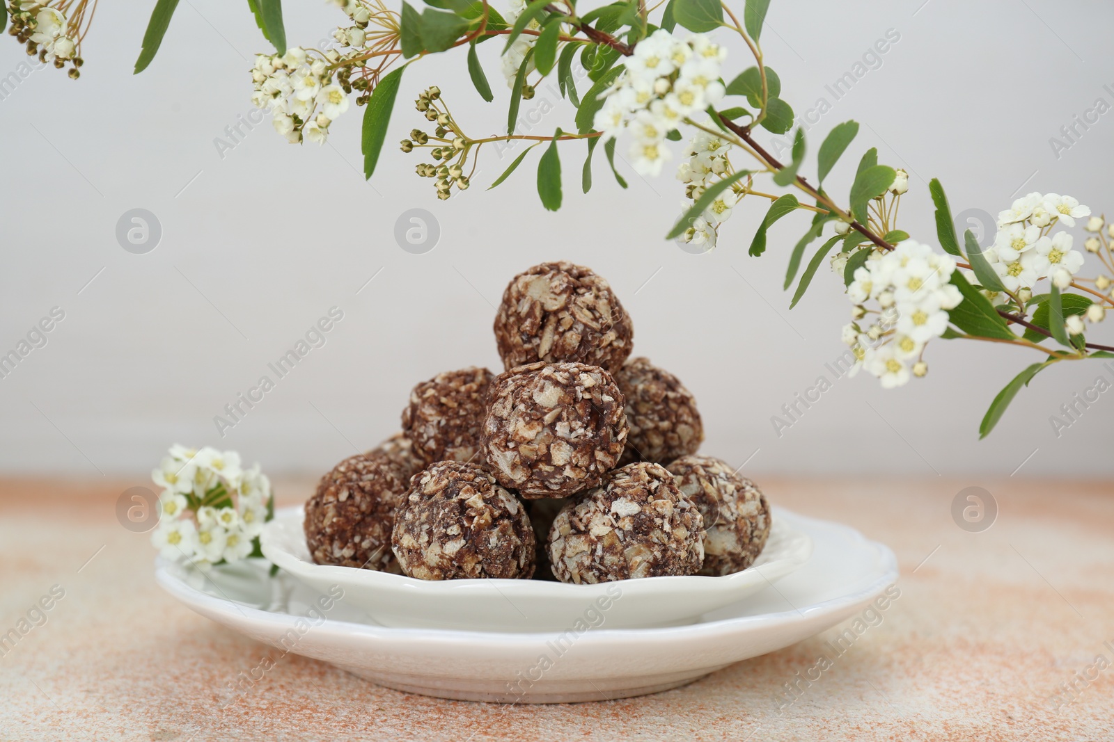 Photo of Delicious chocolate candies under blooming branch on beige table