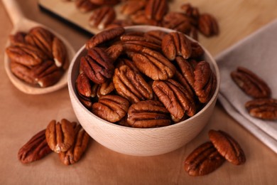 Bowl and tasty pecan nuts on wooden table, closeup