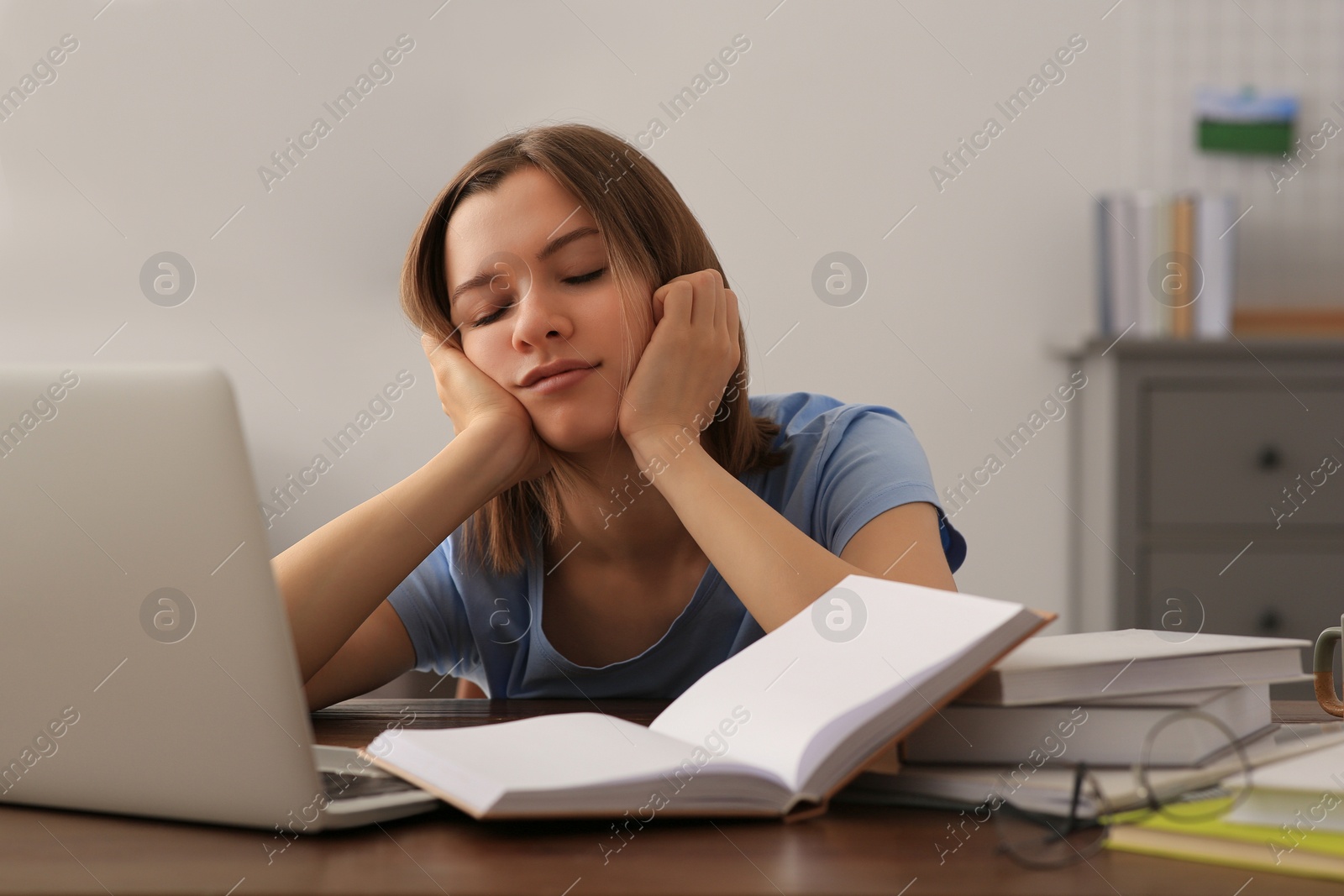 Photo of Young tired woman sleeping near books at wooden table indoors