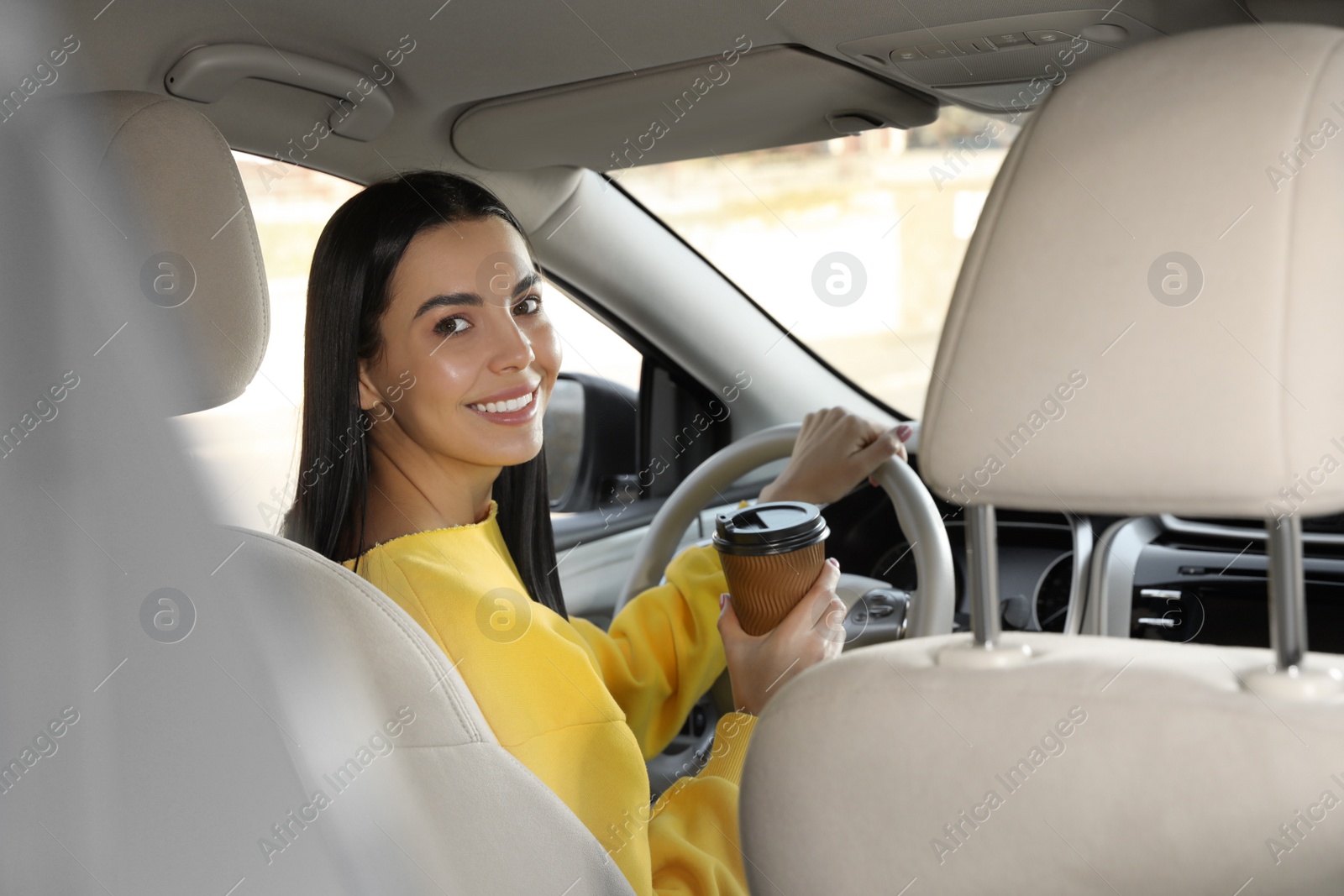 Photo of Beautiful young driver with cup of drink sitting in modern car