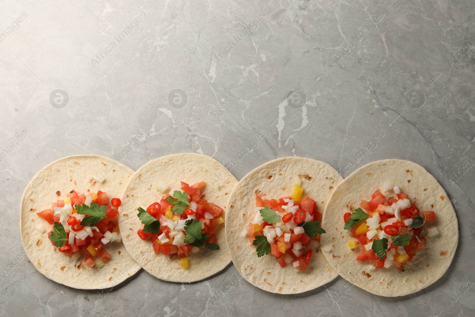 Photo of Delicious tacos with vegetables and parsley on grey marble table, top view. Space for text